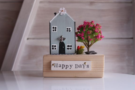 Decorative model house with a tree and the text "Happy Days" on a wooden base.