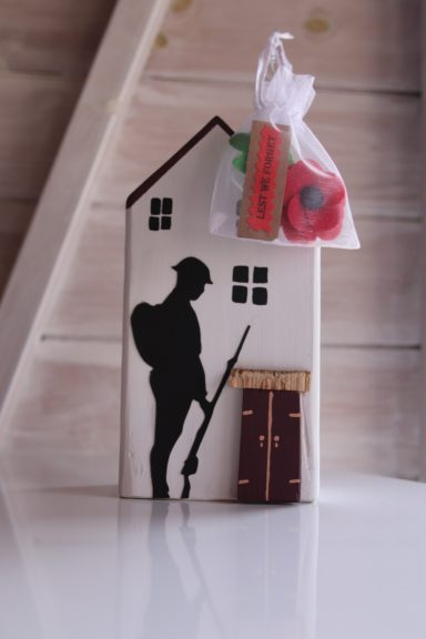 Silhouette of a soldier beside a small house, with a bag of poppies attached.