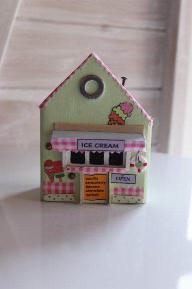 A small green decorative house with an ice cream shop facade and a pink awning.